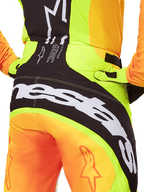 Alpinestars 2025 Techstar Melt Pants, pantaloni da motocross, vista posteriore ravvicinata, giallo neon e arancione con pannelli neri, grande marchio Alpinestars bianco sulla seduta, abbigliamento tecnico per fuoristrada
