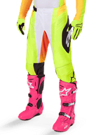Alpinestars 2025 Techstar Melt Pants, pantaloni da motocross, giallo neon con dettagli bianchi e arancioni, motivi laterali neri, indossati con stivali da motocross rosa acceso e guanti giallo neon, con perforazioni per la ventilazione, abbigliamento tecnico resistente per il fuoristrada
