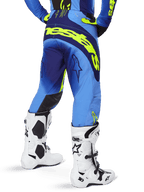 Alpinestars 2025 Techstar Melt Pants, pantaloni da motocross, blu e giallo fluo, vista posteriore con grande marchio giallo sulla seduta e sulle cosce, indossati con stivali da motocross bianchi e maglia blu coordinata, vestibilità atletica da gara per fuoristrada