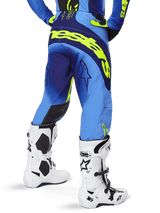 Alpinestars 2025 Techstar Melt Pants, pantaloni da motocross, Giallo Fluo Blu, vista posteriore con grande marchio giallo sulla seduta e dettagli blu scuro, indossati con stivali bianchi Alpinestars Tech 10 e maglia coordinata.