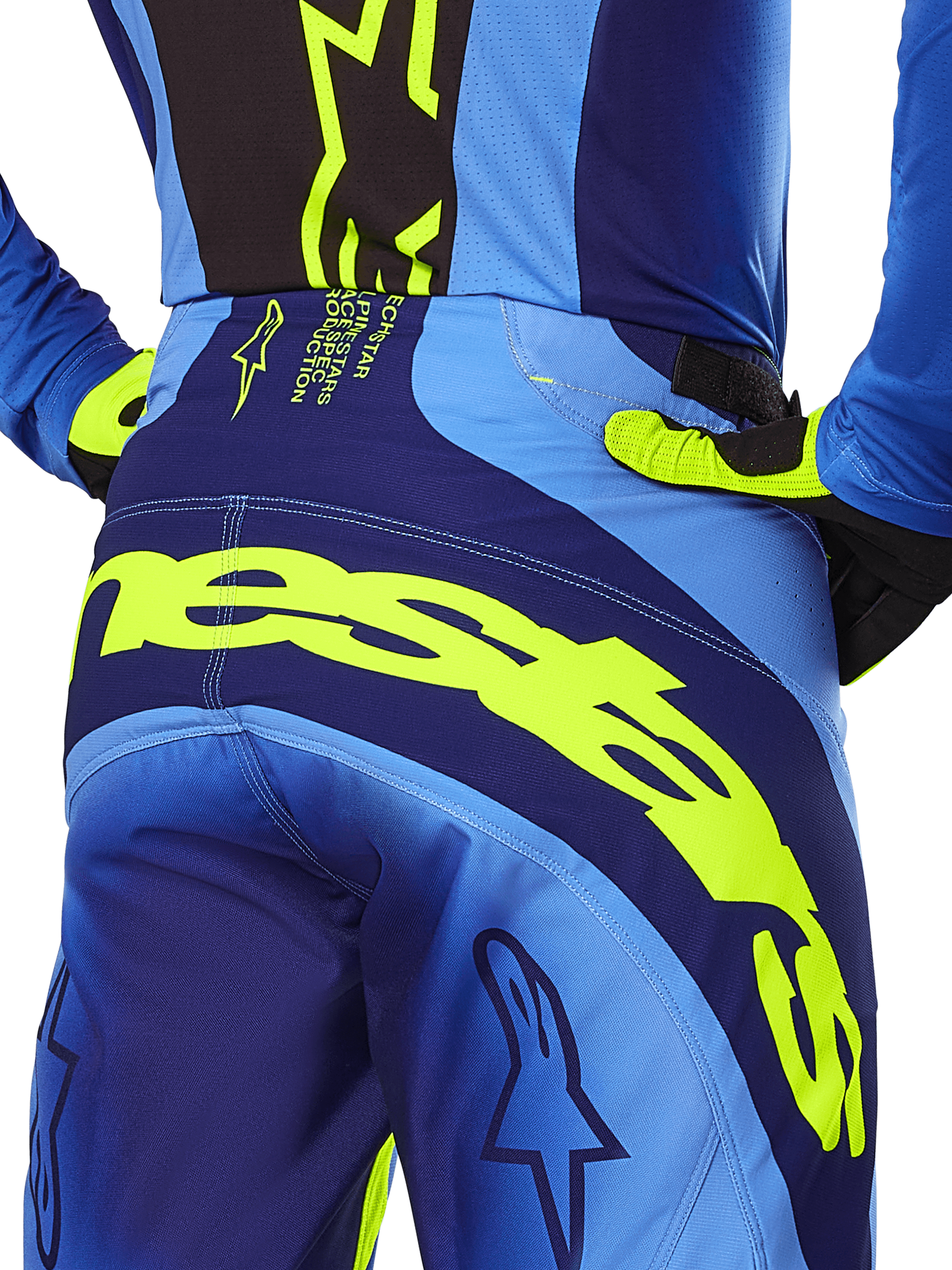 Alpinestars 2025 Techstar Melt Pants, pantaloni da motocross, giallo fluo e blu, primo piano della vista posteriore con vistoso marchio Alpinestars giallo sulla seduta, indossati con maglia blu coordinata e guanti giallo fluo, progettati per corse fuoristrada ad alte prestazioni.