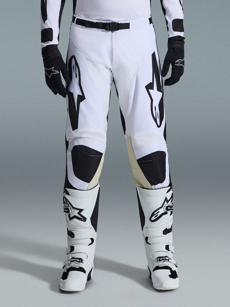 Alpinestars 2026 Racer Riway Pants, pantaloni da motocross, bianco e nero, indossati con stivali da motocross bianchi e neri coordinati e guanti neri, con vistosi loghi Alpinestars neri sulle cosce, design tecnico per prestazioni off-road