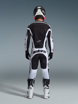 Pantaloni Alpinestars Racer Riway 2026, pantaloni da motocross, bianco e nero, vista posteriore del set completo da gara, vistoso marchio 'astars' sulla seduta, indossati con maglia coordinata, stivali bianchi e casco nero, completo da gara fuoristrada coordinato.