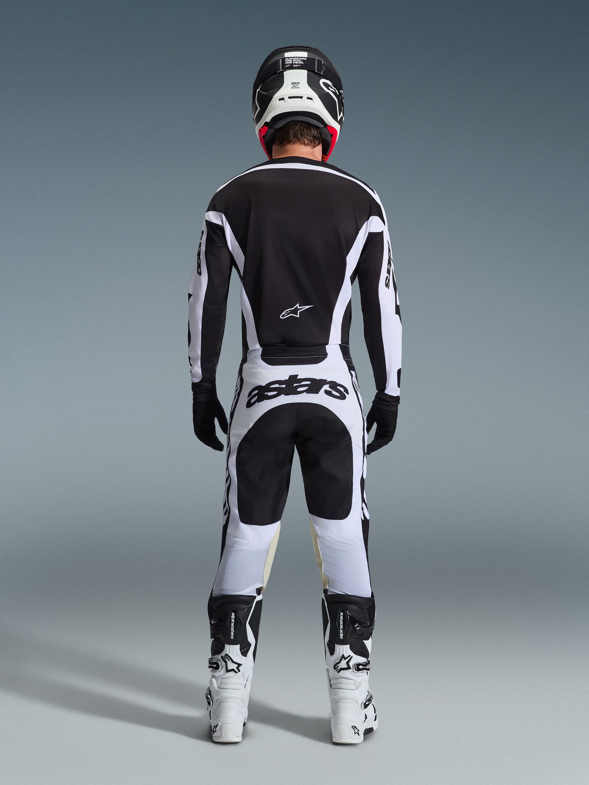 Pantaloni Alpinestars Racer Riway 2026, pantaloni da motocross, bianco e nero, vista posteriore del set completo da gara, vistoso marchio 'astars' sulla seduta, indossati con maglia coordinata, stivali bianchi e casco nero, completo da gara fuoristrada coordinato.