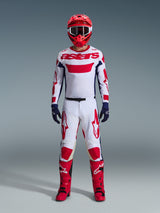 Pilota di motocross con abbigliamento da gara completo, maglia bianca con marchio Alpinestars rosso e dettagli blu, pantaloni Alpinestars 2026 Racer Riway in bianco, blu e rosso, casco rosso con occhiali coordinati, stivali rossi e neri, guanti blu navy, outfit coordinato per corse fuoristrada