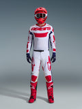 Pilota di motocross che indossa il completo Alpinestars Racer Riway 2026, maglia bianca con marchio "astars" rosso e pannelli laterali blu, pantaloni bianchi con grafiche rosse, casco da gara e stivali rossi, guanti blu scuro, abbigliamento completo coordinato da motocross