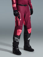 Alpinestars 2026 Racer Riway Pants, pantaloni da motocross, Dark Red Coral, con grandi loghi a stella rosa e pannelli interni neri sulle ginocchia, indossati con stivali da motocross neri e guanti neri, vestibilità atletica da gara per il fuoristrada