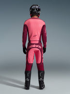 Pilota di motocross visto da dietro che indossa i pantaloni Alpinestars 2026 Racer Riway in Dark Red Coral, maglia coordinata, casco, guanti e stivali neri, con logo 'astars' sulla seduta e design bicolore rosso.