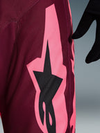 Pantaloni Alpinestars 2026 Racer Riway, pantaloni da motocross, Dark Red Coral, vista ravvicinata che mostra una grande grafica angolare rosa corallo e il logo a stella nero, mettendo in risalto la trama resistente in polyfabric e le cuciture tecniche