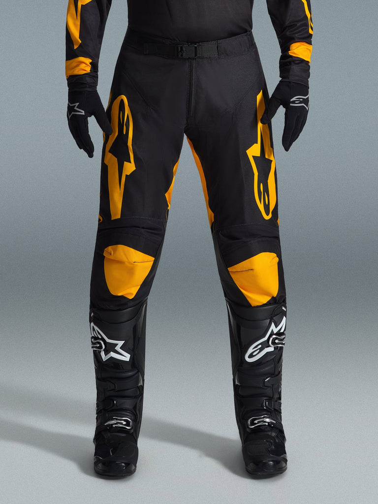 Alpinestars 2026 Racer Riway Pants, pantaloni da motocross, giallo e nero, indossati con guanti da motocross neri e stivali neri con loghi bianchi, con grandi loghi Alpinestars gialli sulle cosce e pannelli gialli sulle ginocchia, design resistente per prestazioni di gara off-road