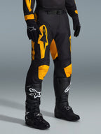 Pantaloni Alpinestars Racer Riway 2026, pantaloni da motocross, giallo e nero, indossati con guanti neri e stivali da motocross neri, con vistoso marchio Alpinestars giallo e inserti sulle ginocchia su base nera, progettati per corse off-road ad alte prestazioni