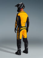 Vista posteriore di un pilota di motocross che indossa i pantaloni Alpinestars 2026 Racer Riway in giallo e nero, maglia coordinata, casco nero e stivali neri, set completo di abbigliamento da gara coordinato per prestazioni off-road