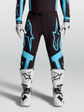 Alpinestars Pantaloni Supertech Vesta, pantaloni da motocross professionali, nero e turchese, grafica a stella, pannelli sulle ginocchia in pelle, indossati con stivali e guanti bianchi
