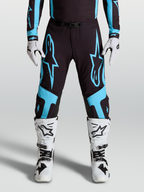 Alpinestars Pantaloni Supertech Vesta, pantaloni da motocross professionali, nero e turchese, grafica a stella, pannelli sulle ginocchia in pelle, indossati con stivali e guanti bianchi