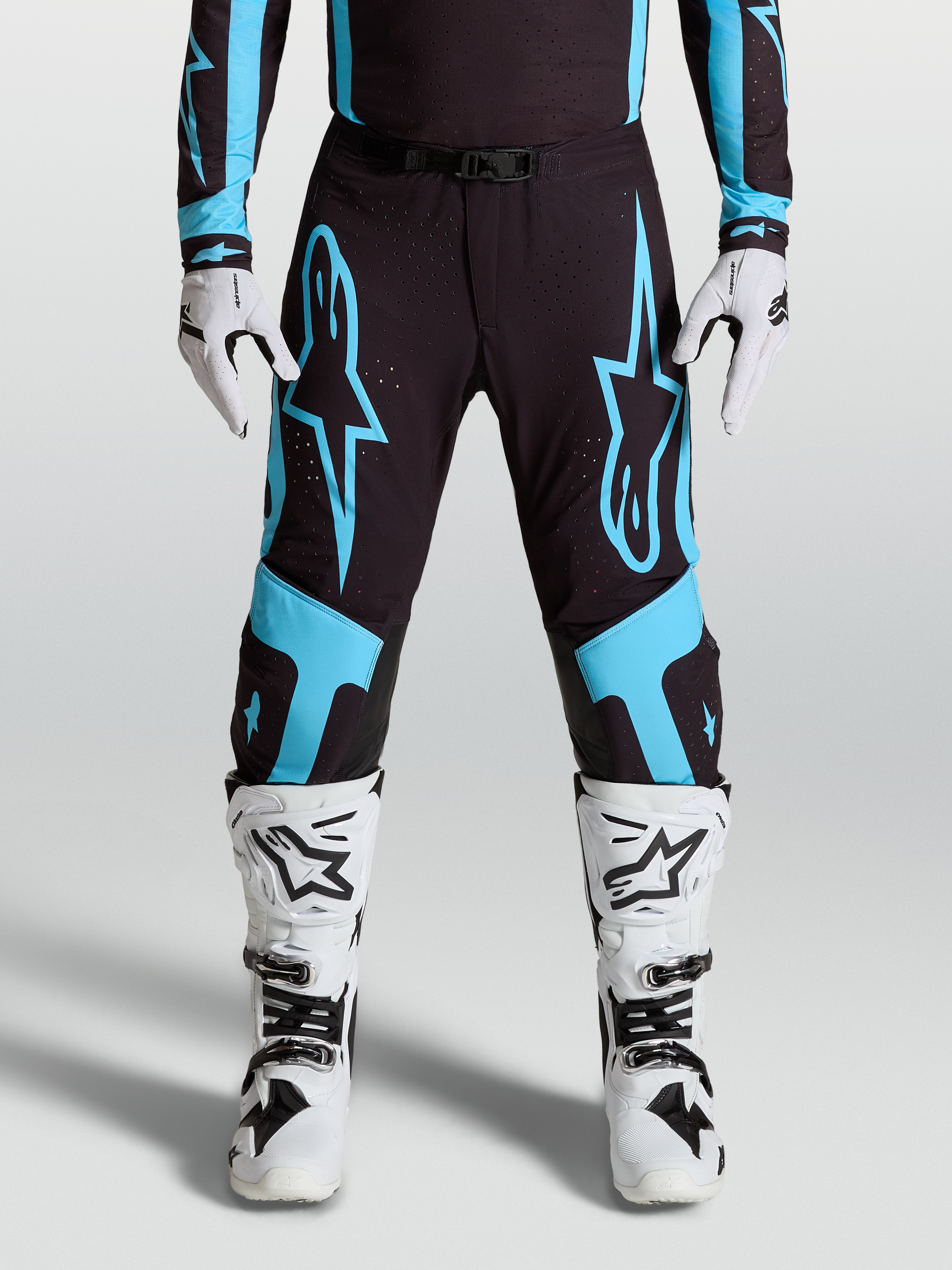 Alpinestars Pantaloni Supertech Vesta, pantaloni da motocross professionali, nero e turchese, grafica a stella, pannelli sulle ginocchia in pelle, indossati con stivali e guanti bianchi