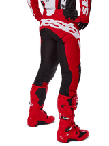 Alpinestars 2025 Racer Veil Pants, pantaloni da motocross, nero e rosso acceso, vista posteriore con grande logo Alpinestars bianco sulla seduta, pannelli elasticizzati neri sul retro delle gambe, indossati con stivali da corsa rossi coordinati, abbigliamento da gara off-road resistente