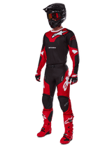 Alpinestars 2025 Racer Veil Pants, pantaloni da motocross, nero e rosso brillante, indossati come parte di un set completo di abbigliamento da gara con maglia coordinata, casco nero, occhiali rossi e stivali rossi, outfit coordinato per prestazioni off-road.