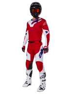 Alpinestars 2025 Racer Veil Pants, pantaloni da motocross, rosso acceso e bianco, indossati come parte di un set completo da gara con maglia coordinata rossa e bianca, casco nero con occhiali arancioni, stivali bianchi e guanti rossi, con loghi Alpinestars blu vivace.