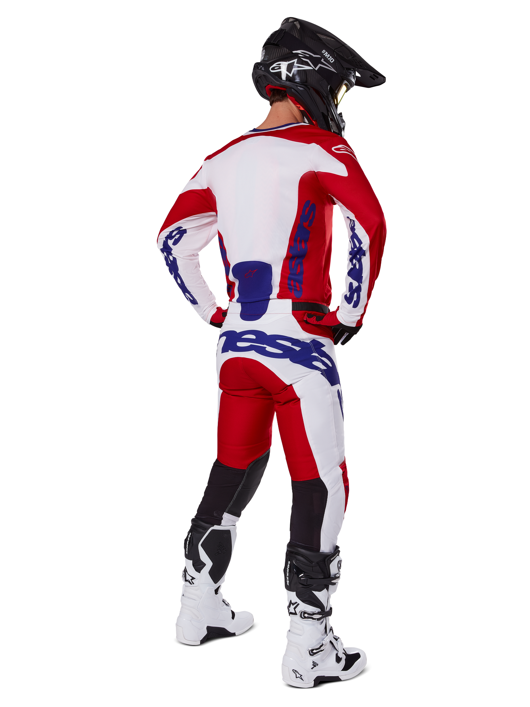 Pantaloni Alpinestars Racer Veil 2025, pantaloni da motocross, rosso e bianco con accenti blu, visti da dietro su un pilota con attrezzatura completa, logo Alpinestars audace, pannelli traspiranti sulla parte inferiore delle gambe, stivali bianchi e casco nero coordinati.