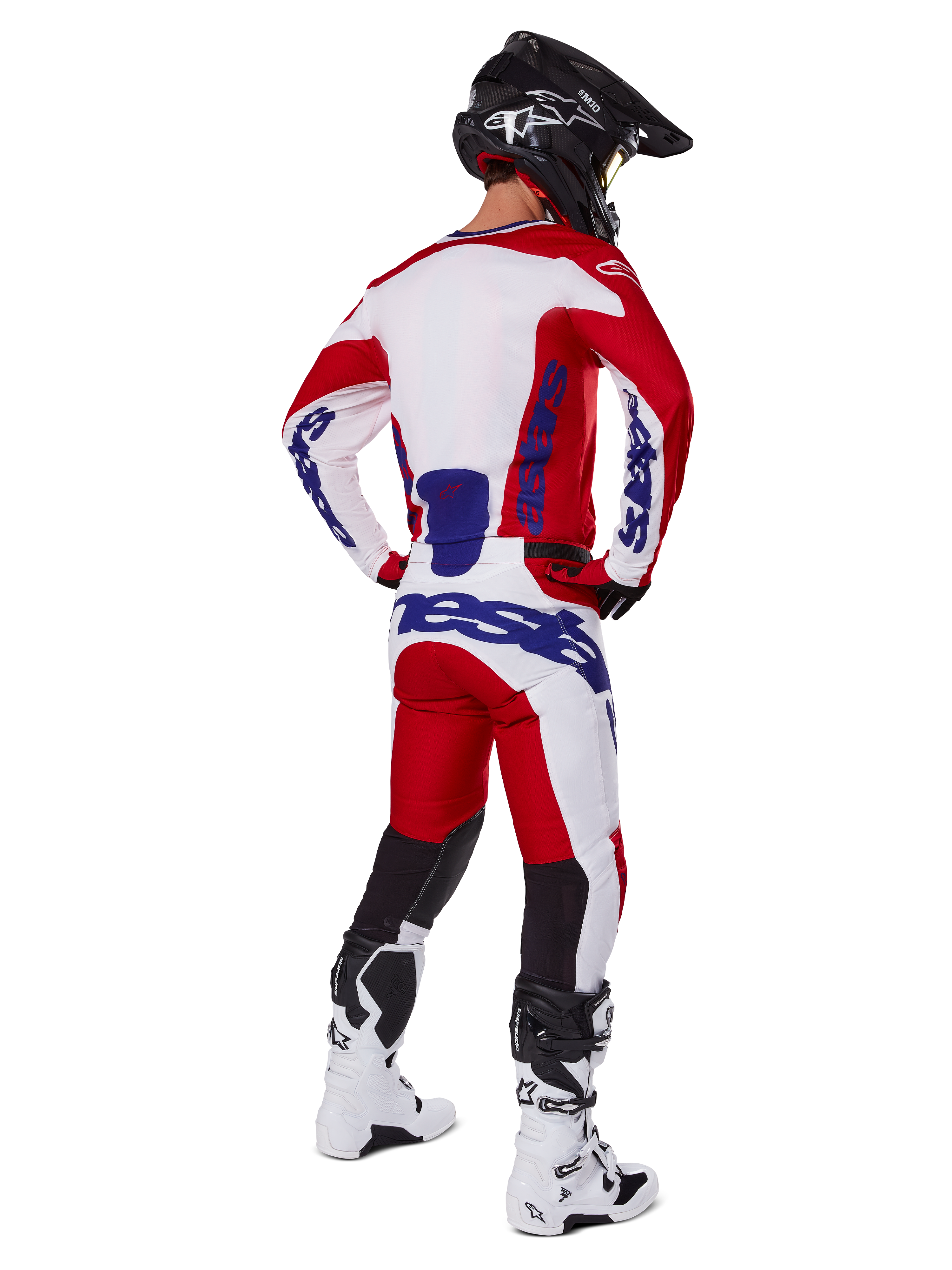 Pantaloni Alpinestars Racer Veil 2025, pantaloni da motocross, rosso e bianco con accenti blu, visti da dietro su un pilota con attrezzatura completa, logo Alpinestars audace, pannelli traspiranti sulla parte inferiore delle gambe, stivali bianchi e casco nero coordinati.