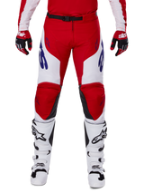 Alpinestars 2025 Racer Veil Pants, pantaloni da motocross, rosso acceso e bianco, indossati con guanti rossi abbinati e stivali bianchi, con branding blu sulle cosce e cintura nera in vita, taglio sportivo ergonomico per prestazioni elevate