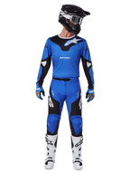Pantaloni Alpinestars Racer Veil 2025, pantaloni da motocross, blu e nero, indossati come completo da corsa con maglia coordinata blu e nera, casco nero e bianco, guanti blu e stivali bianchi, con loghi audaci e design ergonomico per la guida fuoristrada.