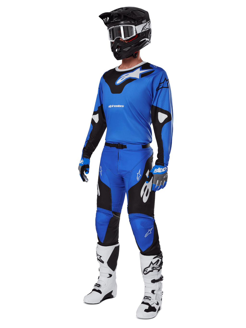 Pilota di motocross con abbigliamento da gara completo, inclusi pantaloni Alpinestars Racer Veil 2025 blu e neri, maglia blu coordinata con dettagli bianchi, casco nero con occhiali bianchi, stivali bianchi e neri e guanti blu, completo coordinato per gare off-road