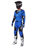 Pilota di motocross con abbigliamento da gara completo, inclusi pantaloni Alpinestars Racer Veil 2025 blu e neri, maglia blu coordinata con dettagli bianchi, casco nero con occhiali bianchi, stivali bianchi e neri e guanti blu, completo coordinato per gare off-road