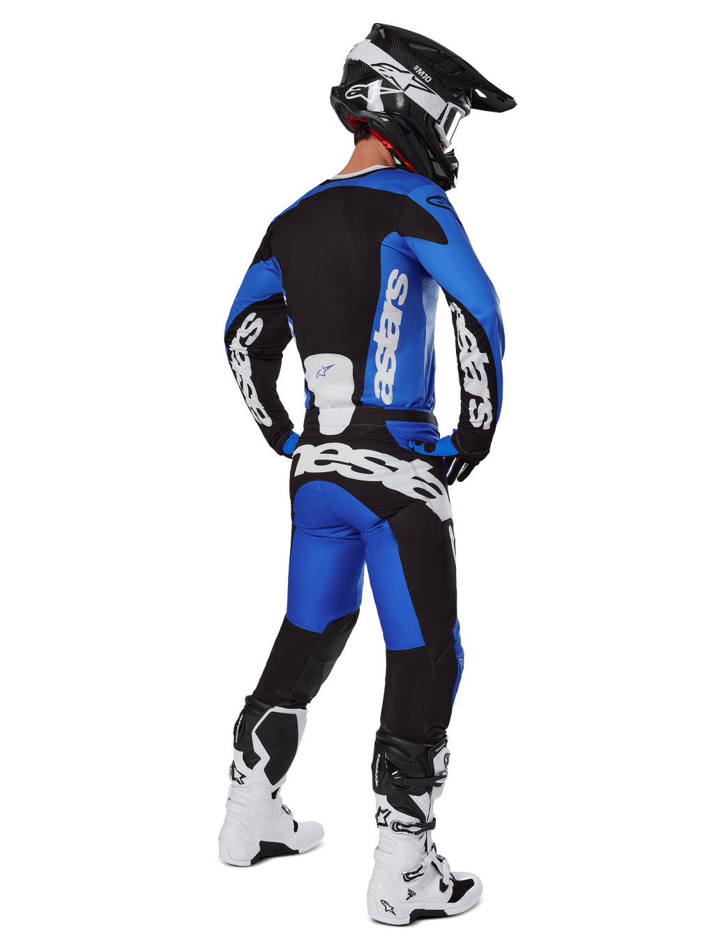 Pilota di motocross visto da dietro che indossa pantaloni Alpinestars Racer Veil 2025 blu e neri, maglia a maniche lunghe coordinata con logo bianco, stivali Tech 7 bianchi e neri e casco SM10 nero, set completo di abbigliamento per corse fuoristrada