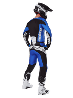 Pilota di motocross visto da dietro che indossa pantaloni Alpinestars Racer Veil 2025 blu e neri, maglia a maniche lunghe coordinata con logo bianco, stivali Tech 7 bianchi e neri e casco SM10 nero, set completo di abbigliamento per corse fuoristrada
