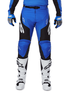 Pantaloni Alpinestars Racer Veil 2025, pantaloni da motocross, blu e nero, con loghi Alpinestars bianchi sulle gambe e pannelli laterali neri, indossati con stivali da motocross bianchi e guanti blu e grigi, abbigliamento tecnico per il fuoristrada.