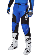 Alpinestars 2025 Racer Veil Pants, pantaloni da motocross, blu e nero con dettagli grafici bianchi, indossati con maglia e guanti blu coordinati e stivali bianchi, attrezzatura protettiva resistente per gare fuoristrada