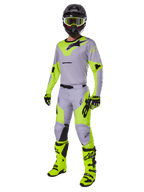Pantaloni Alpinestars Racer Veil 2025, pantaloni da motocross, grigio e giallo fluo, indossati con maglia coordinata, casco nero, maschera giallo fluo, stivali e guanti, completo da gara off-road coordinato con design ergonomico e loghi evidenti.