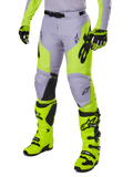 Alpinestars 2025 Racer Veil Pants, pantaloni da motocross, grigio e giallo neon fluo, con loghi a stella neri e cintura regolabile in vita, mostrati con stivali e guanti da motocross coordinati, design ergonomico per la guida off-road