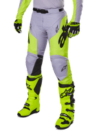 Alpinestars 2025 Racer Veil Pants, pantaloni da motocross, grigio e giallo neon fluo, con loghi a stella neri e cintura regolabile in vita, mostrati con stivali e guanti da motocross coordinati, design ergonomico per la guida off-road