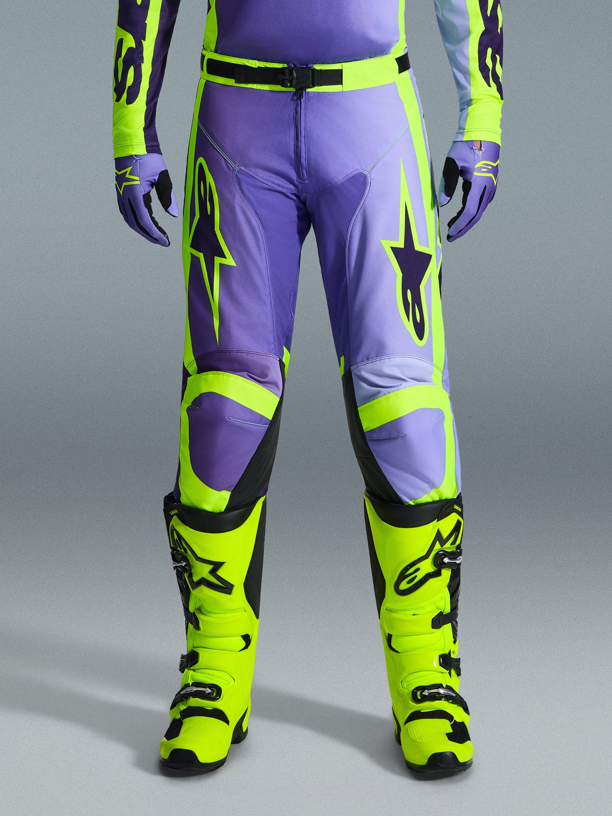 Alpinestars 2026 Racer Portl Pants, pantaloni da motocross, viola e giallo fluo, indossati con stivali giallo fluo e guanti viola coordinati, caratterizzati da grandi loghi a stella e struttura in poliestere resistente per corse fuoristrada