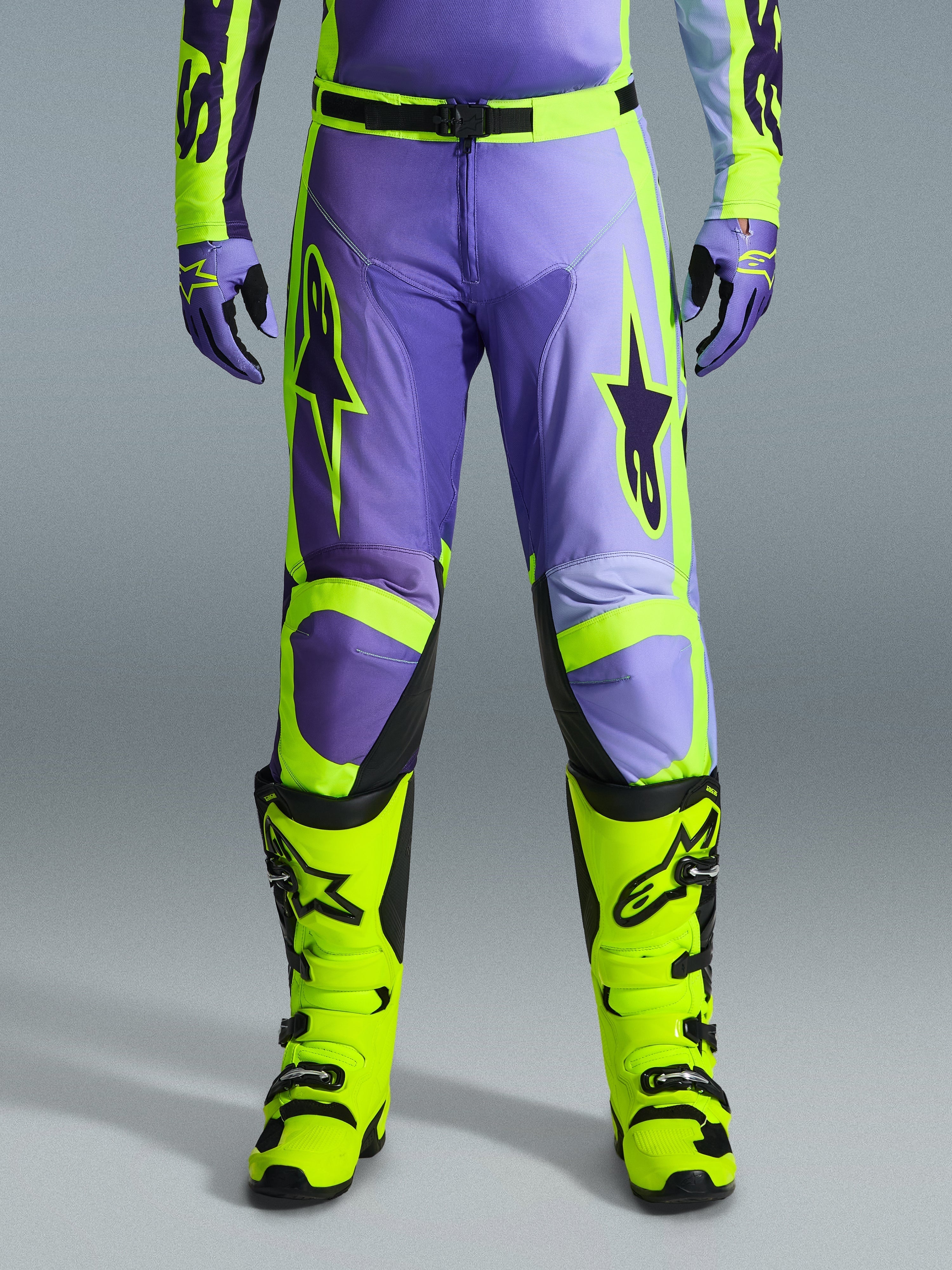 Alpinestars 2026 Racer Portl Pants, pantaloni da motocross, viola e giallo fluo, indossati con stivali giallo fluo e guanti viola coordinati, caratterizzati da grandi loghi a stella e struttura in poliestere resistente per corse fuoristrada