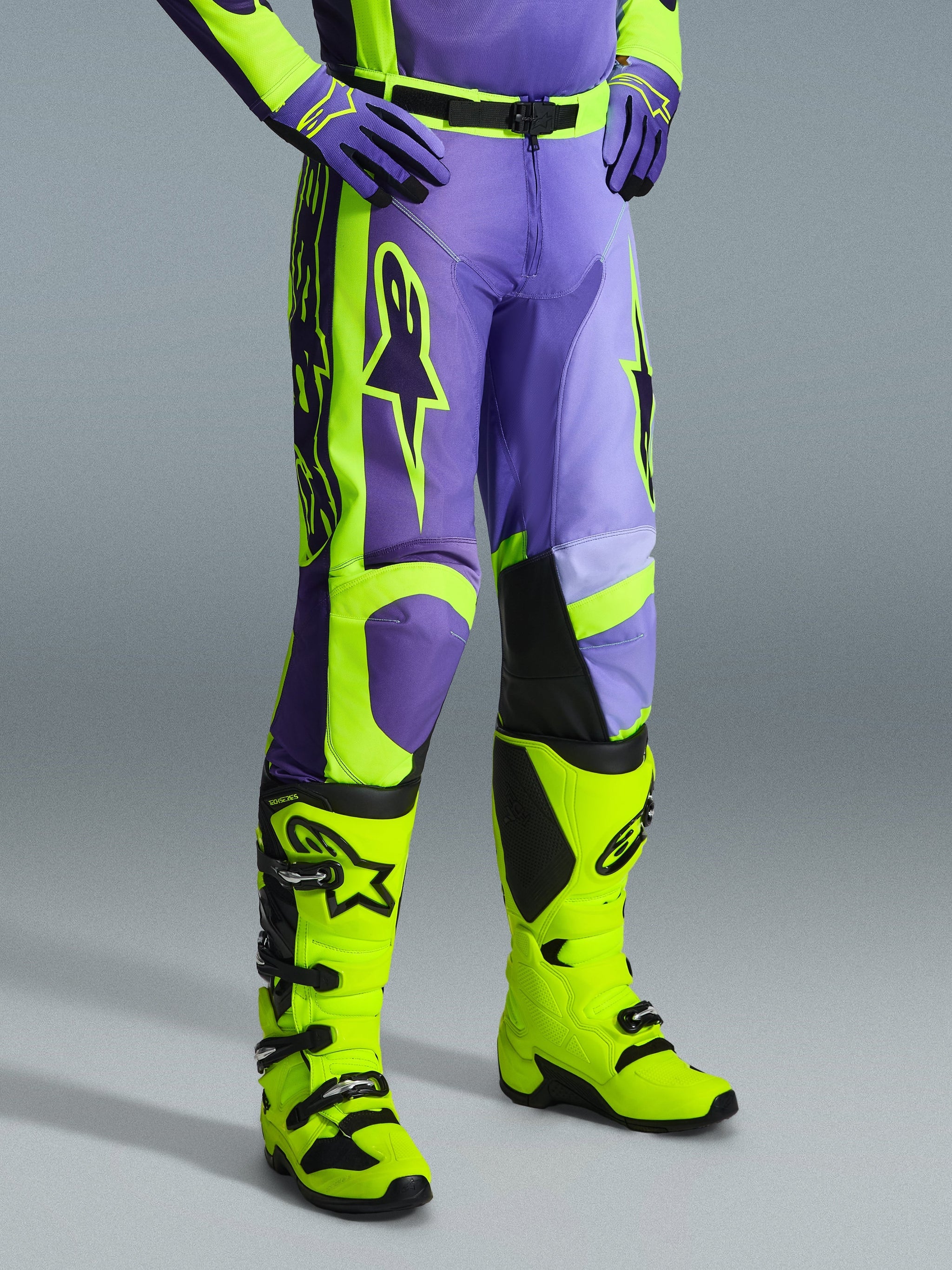Alpinestars 2026 Racer Portl Pants, pantaloni da motocross viola e giallo fluo, indossati da un pilota con stivali giallo fluo e guanti viola coordinati, con branding Alpinestars evidente e design ergonomico per prestazioni fuoristrada