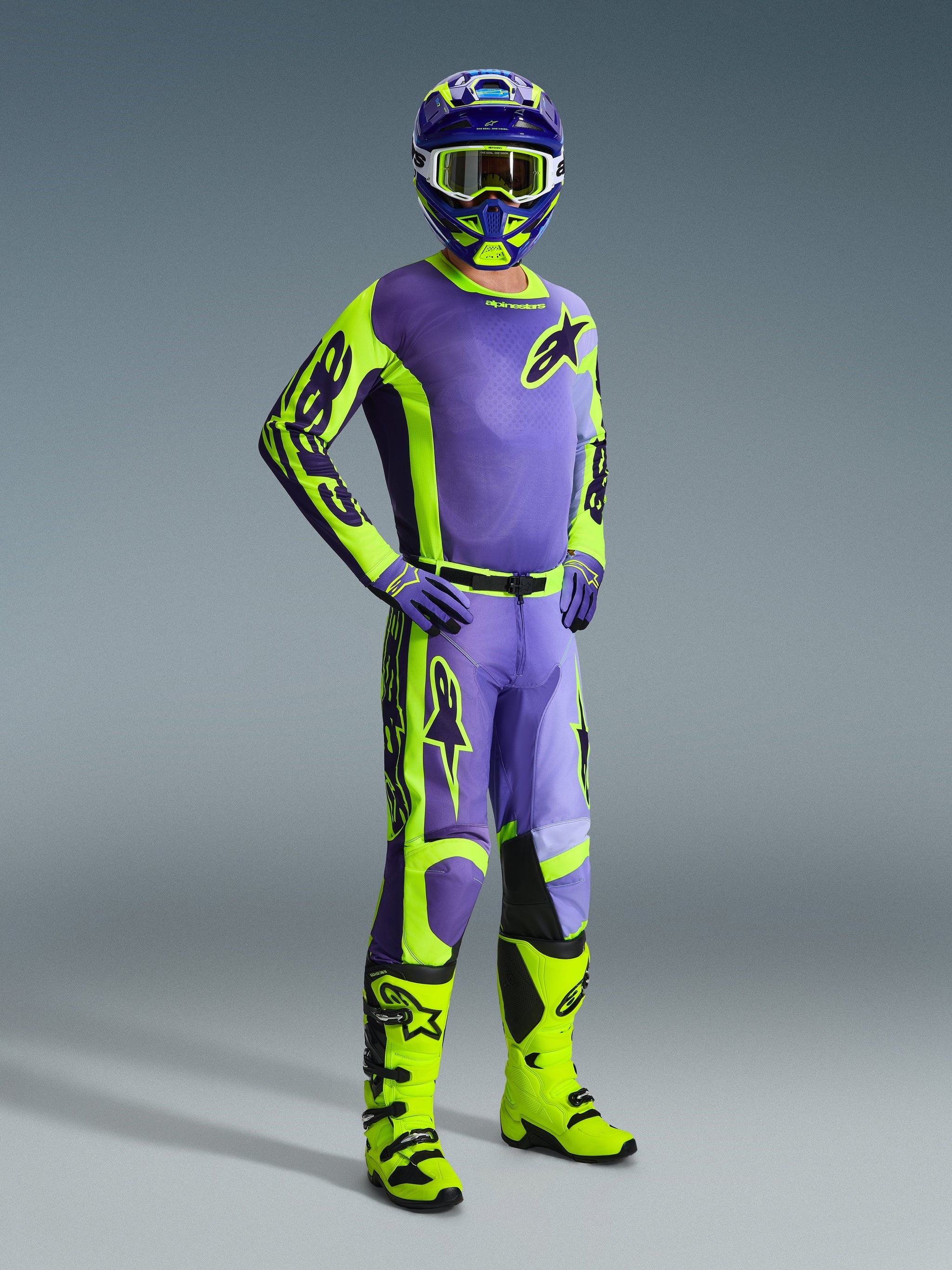 Pilota di motocross con attrezzatura Alpinestars Racer Portl 2026, maglia e pantaloni viola e giallo fluo, stivali giallo neon, guanti viola e casco coordinato, outfit completo per prestazioni motocross off-road.