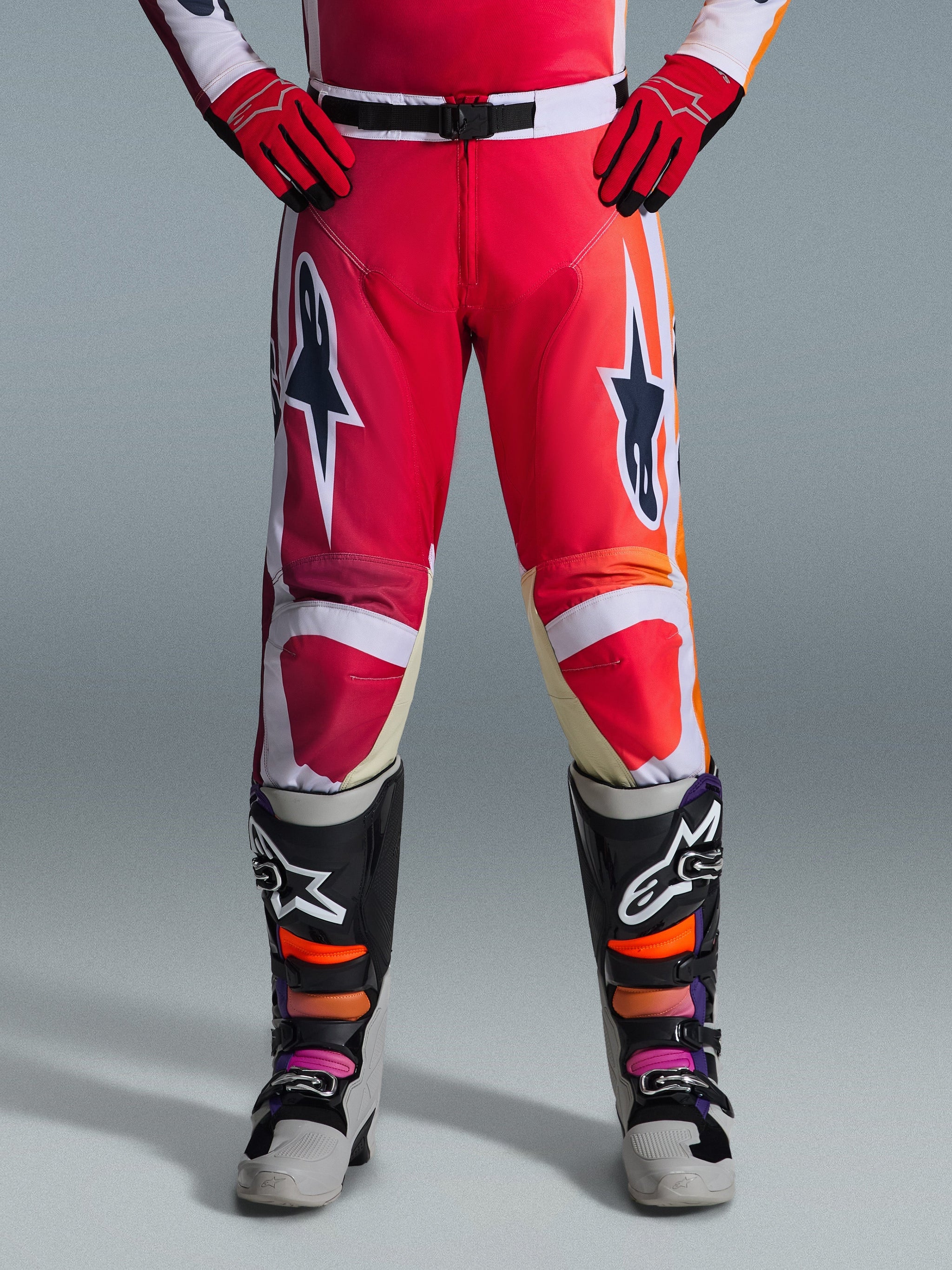 Alpinestars 2026 Racer Portl Pants, pantaloni da motocross, rosso, grigio chiaro e grigio scuro, indossati con guanti rossi coordinati e stivali multicolore, caratterizzati da grandi loghi a stella Alpinestars sulle cosce e dettagli bianchi, design sportivo per corse fuoristrada