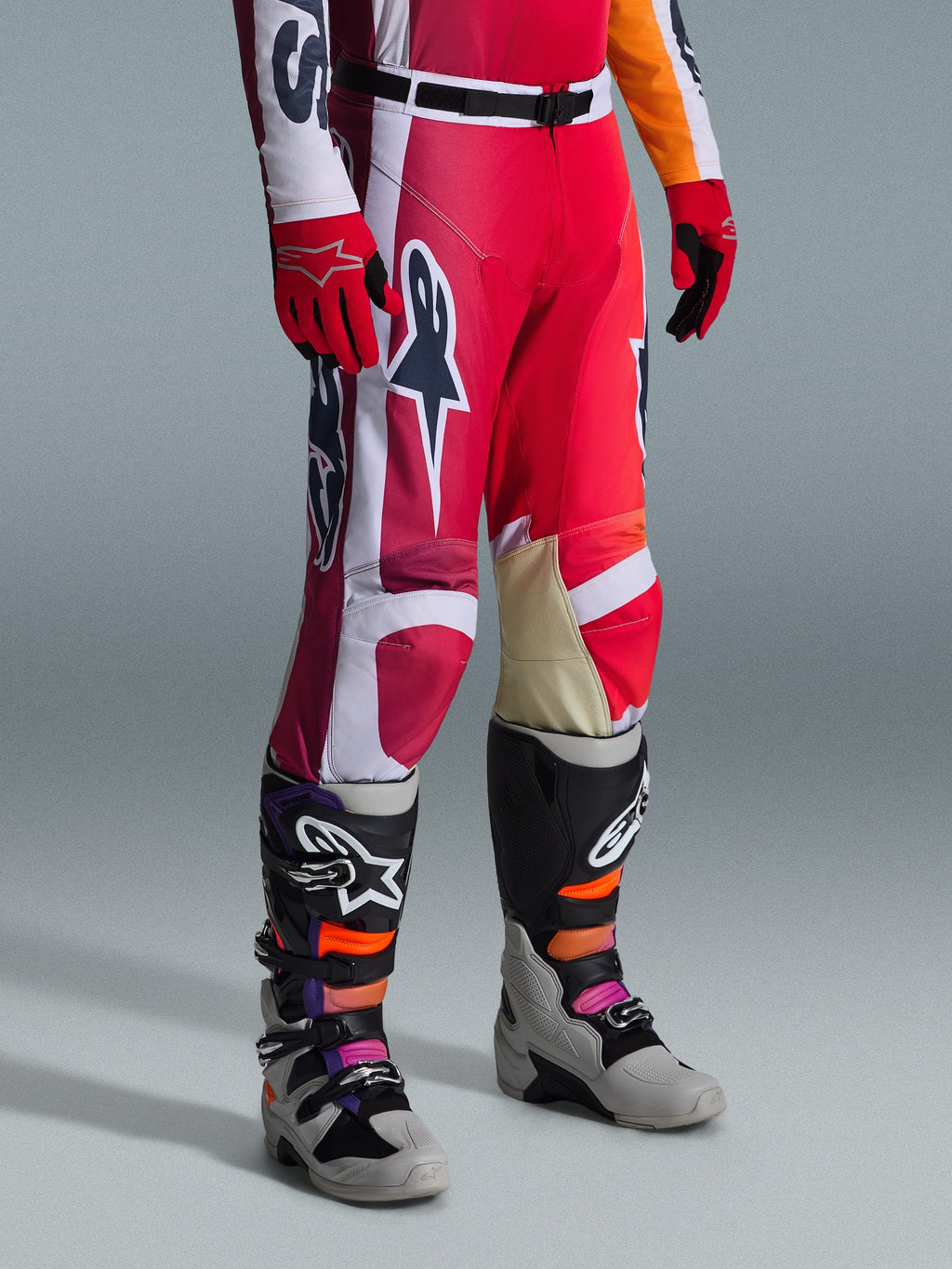 Pantaloni Alpinestars 2026 Racer Portl, pantaloni da motocross, rosso, grigio chiaro e grigio scuro, indossati con guanti rossi coordinati e stivali da motocross multicolore, con loghi Alpinestars e pannelli rinforzati per corse off-road.