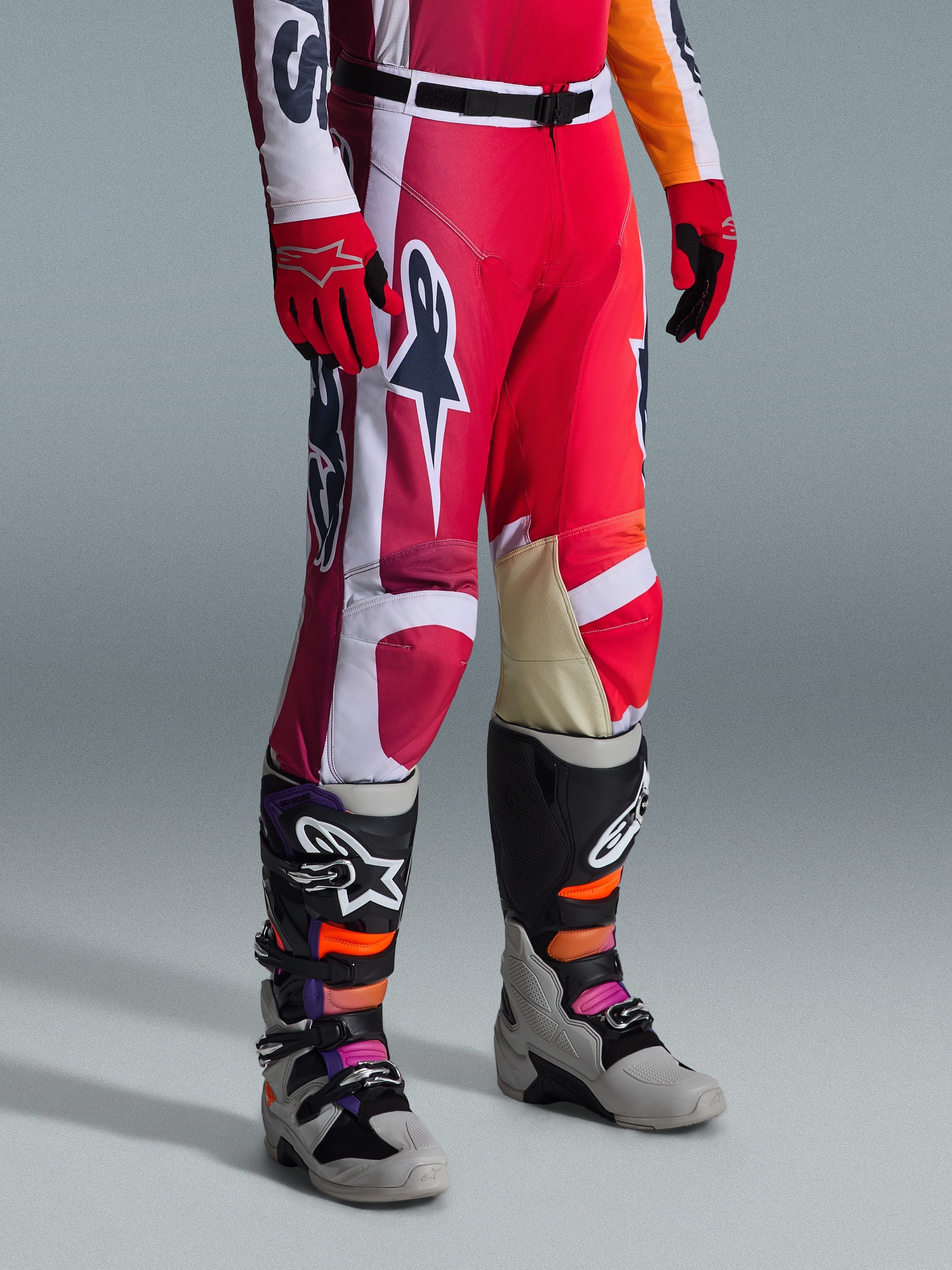 Pantaloni Alpinestars 2026 Racer Portl, pantaloni da motocross, rosso, grigio chiaro e grigio scuro, indossati con guanti rossi coordinati e stivali da motocross multicolore, con loghi Alpinestars e pannelli rinforzati per corse off-road.