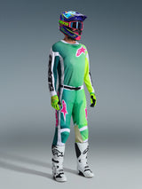 Pilota di motocross con pantaloni Alpinestars 2026 Racer Portl e maglia coordinata in verde, bianco e nero con accenti rosa nel logo, casco colorato, stivali da gara bianchi e neri e guanti verde neon, set completo per corse off-road