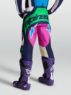 Alpinestars Pantaloni Techstar Maven, pantaloni motocross da uomo, blu e verde con dettagli fucsia, vista posteriore su modello con stivali Tech 10 viola.