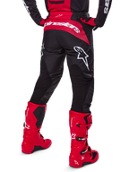 Alpinestars Set Gear Fluid Haul 2025, vista posteriore, pantaloni da motocross neri e rossi con grandi loghi bianchi, maglia coordinata e stivali Tech 7 in rosso vivace, kit da gara fuoristrada coordinato