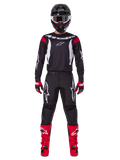Alpinestars 2025 Fluid Haul Gear Set, pilota di motocross in abbigliamento completo, maglia nera con dettagli rossi sulle spalle e loghi bianchi, pantaloni neri con logo a stella bianco, stivali rosso acceso, guanti rossi e neri, casco nero con occhiali bianchi, look coordinato per prestazioni off-road