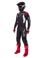 Pilota da motocross con set completo Alpinestars 2025 Fluid Haul, maglia nera con dettagli rossi e bianchi, pantaloni neri con loghi bianchi, stivali rosso acceso, guanti rossi e neri, casco nero con maschera, abbigliamento tecnico coordinato per fuoristrada