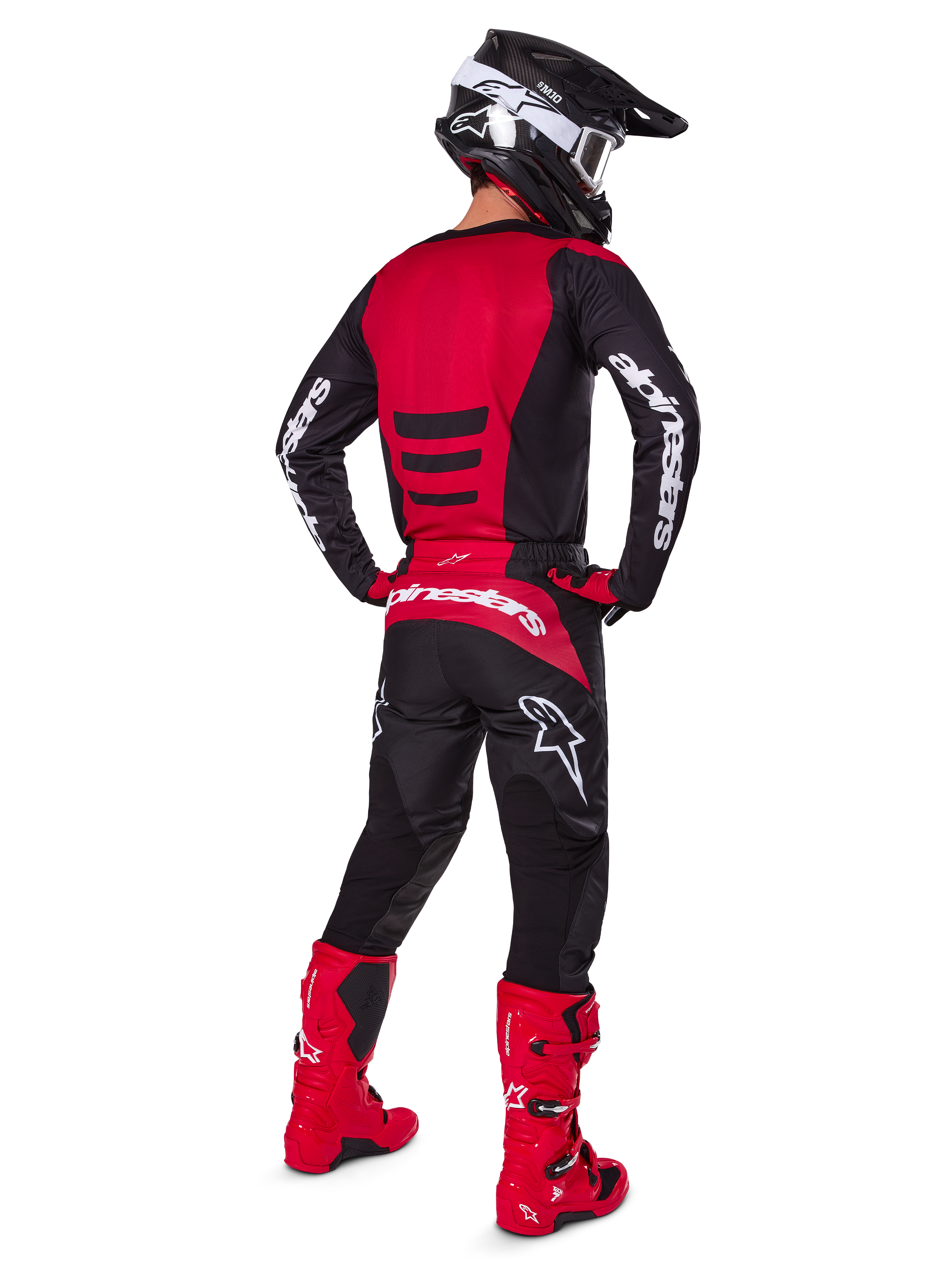 Pilota di motocross con il Set Gear Alpinestars 2025 Fluid Haul visto da dietro, maglia rossa e nera con logo bianco, pantaloni neri coordinati con accenti rossi, stivali rosso acceso e casco nero con occhiali bianchi, outfit completo coordinato per gare off-road
