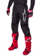 Alpinestars 2025 Fluid Haul Pants, pantaloni da motocross, nero, con un grande logo Alpinestars bianco, indossati con stivali rosso acceso e guanti rossi e neri, costruzione resistente in poliestere 600D con taglio ergonomico per il fuoristrada