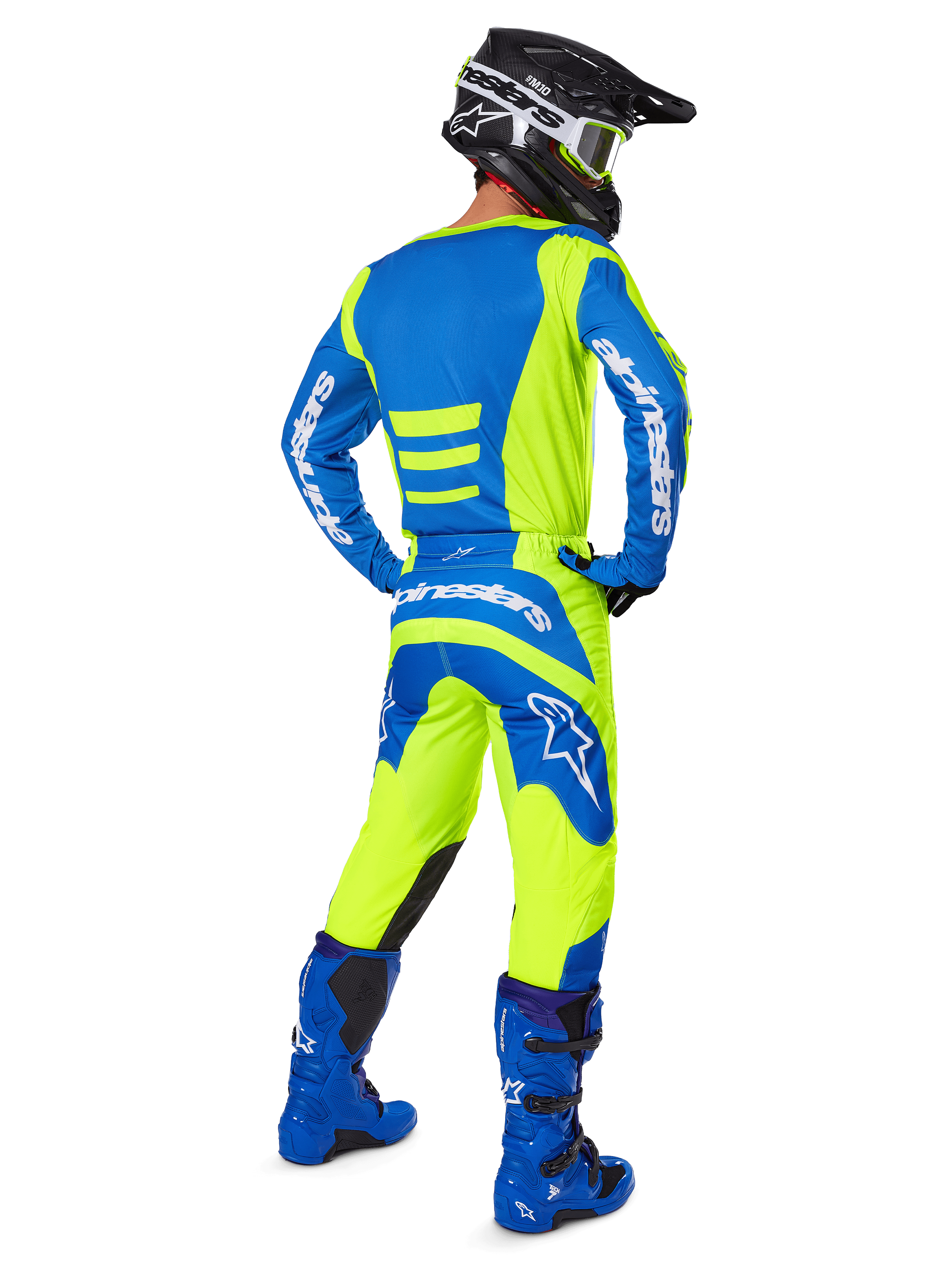 Pilota di motocross visto da dietro che indossa i pantaloni Alpinestars 2025 Fluid Haul e la maglia coordinata in Giallo Fluo e Blu, abbinati a stivali blu e casco nero Alpinestars, equipaggiamento professionale per gare fuoristrada